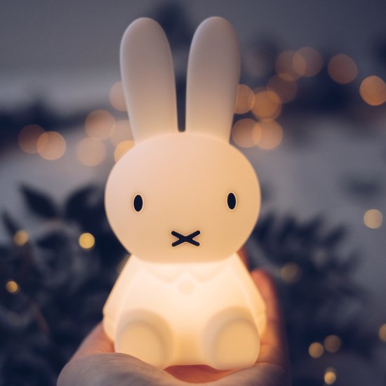 Een hand houdt een verlicht, wit Miffy-lampje vast met bokeh-lichtjes op de achtergrond.