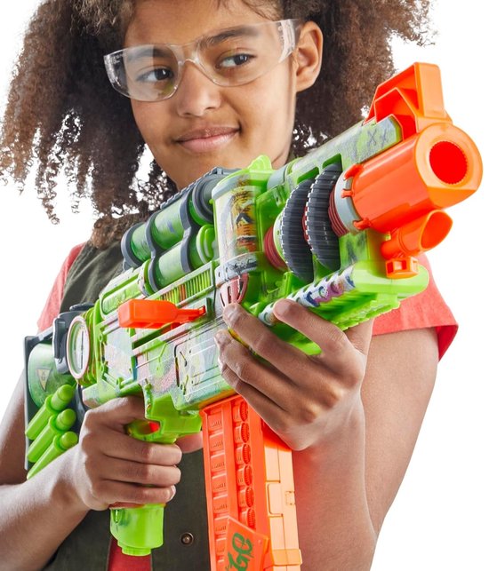 Meisje met beschermende bril richt een felgroene Nerf Zombie Corrupter blaster met oranje accenten naar de camera.
