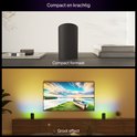 Une lampe Philips Hue Play noire sur une table et deux lampes projetant de la lumière derrière une télévision.