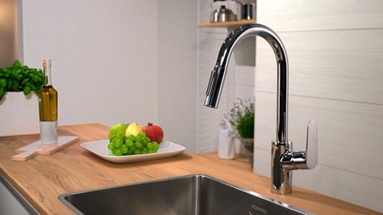 Robinet de cuisine brillant avec douchette extractible au-dessus d'un évier, à côté de fruits.