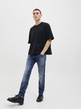 Man in een zwart oversized T-shirt, blauwe jeans en zwarte schoenen, met één been naar voren.