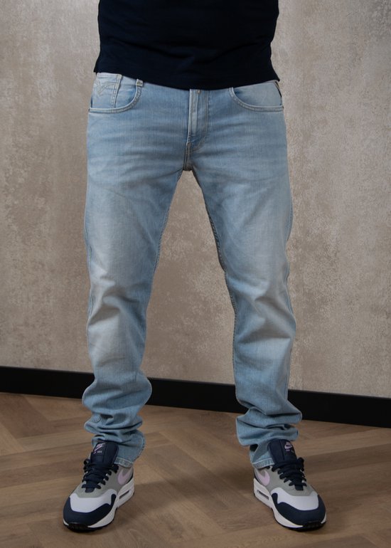 Homme portant un jean Replay bleu clair délavé et des baskets bleu-gris.