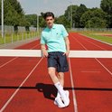 Man in een lichtgroene polo en donkerblauwe Donnay sportbroek op een atletiekbaan.