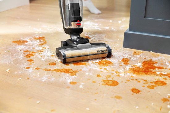 De BISSELL CrossWave reinigt een houten vloer met oranje vlekken en witte kruimels.
