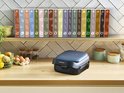 Een gesloten, donkergrijs Tefal wafelijzer staat op een houten aanrecht met diverse Tefal Snack Collection dozen op de achtergrond.