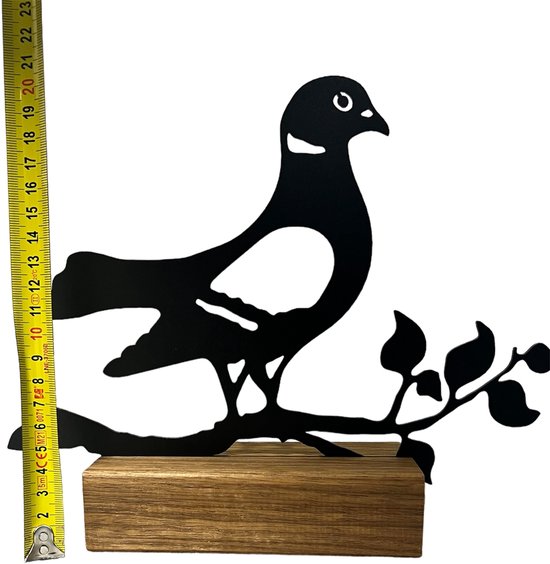 Zwart metalen duif met tak en bladeren op een houten sokkel, naast een rolmaat. Totale hoogte ca. 20cm.