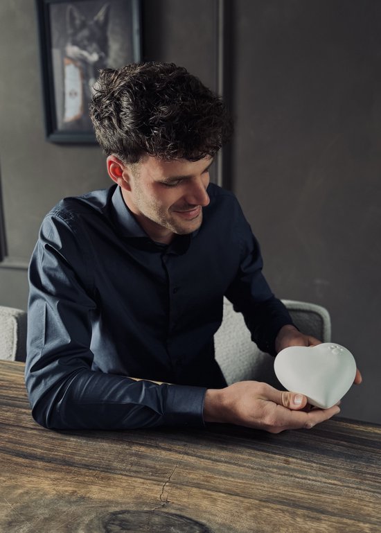 Man met krullend haar, kijkend naar een wit hartvormig object in zijn handen.