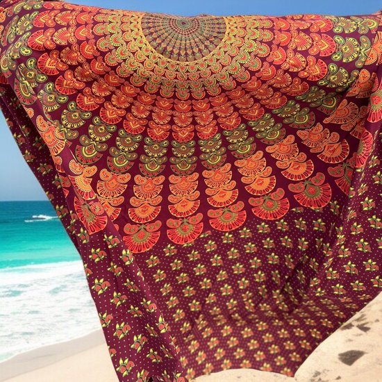 Paars strandkleed met oranje, rode en gele mandala print. Hangt voor een blauwe lucht en zee.