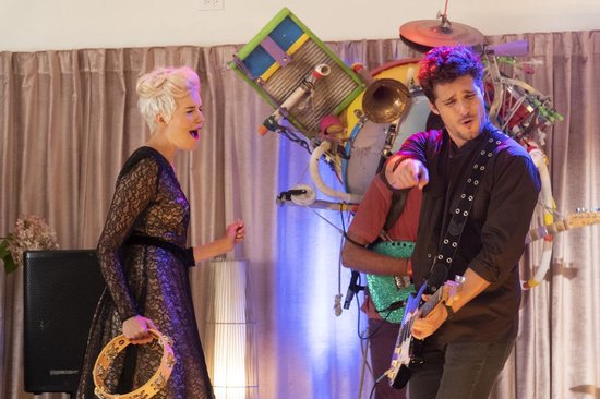 Megalyn Echikunwoke in zwart kanten jurk met tamboerijn, naast Diego Boneta die gitaar speelt in een band.