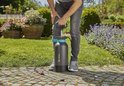 Een man in grijze spijkerbroek gebruikt een zwarte GARDENA drukspuit met blauwe details in de tuin.