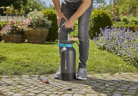 Een man in grijze spijkerbroek gebruikt een zwarte GARDENA drukspuit met blauwe details in de tuin.