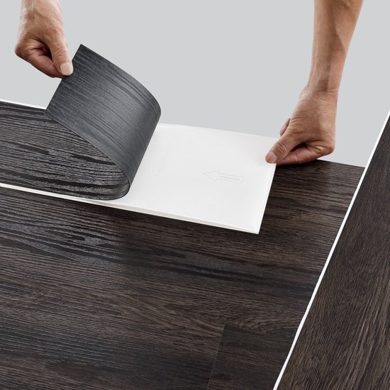 Handen die de beschermlaag van een donkerbruine PVC vloerplank met houtnerf aftrekken.