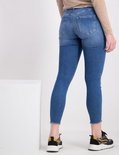 Achterkant van een model die een skinny jeans draagt, met rafelige zoom en een lichtblauwe denim wassing.