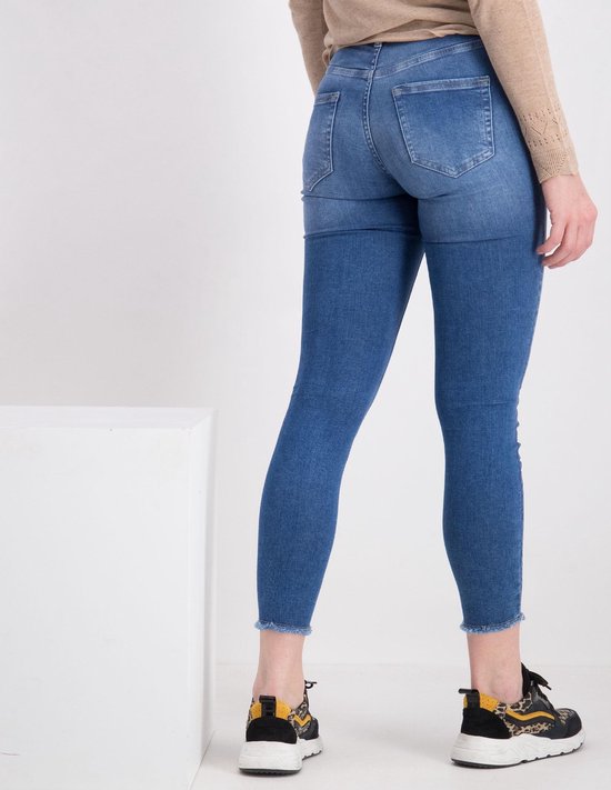 Achterkant van een model die een skinny jeans draagt, met rafelige zoom en een lichtblauwe denim wassing.