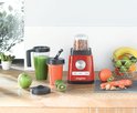 Rode Magimix blender met noten in de beker, naast smoothies, fruit en groenten.