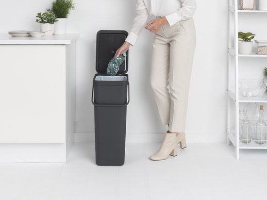 Une femme jette une bouteille dans une poubelle grise avec seau intérieur.