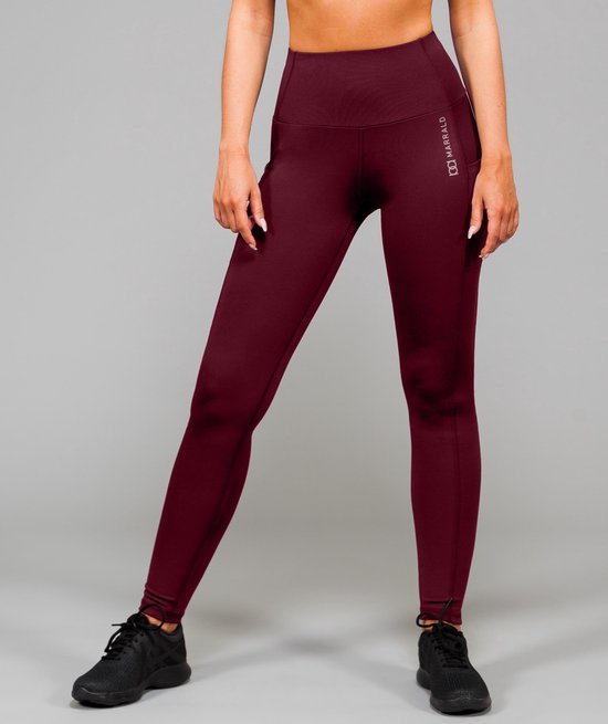 Een model draagt een bordeauxrode sportlegging van Marrald met hoge taille en zakken, met een zilverkleurig logo op de linkerheup en zwarte sportschoenen.