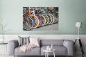Une rangée de vélos colorés avec des jantes orange, bleues, blanches, roses et jaunes, au-dessus d'un canapé dans un salon.