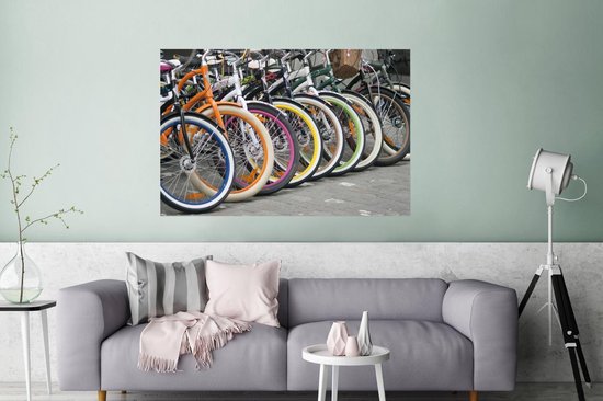 Une rangée de vélos colorés avec des jantes orange, bleues, blanches, roses et jaunes, au-dessus d'un canapé dans un salon.