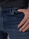 Close-up van de voorkant van een donkerblauwe jeans met lichte wassing, inclusief zakken en knopen.