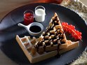 Wafel met chocoladesaus, poedersuiker, slagroom, rode bessen en een kannetje melk en aardbeiensaus.