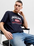 Zittende man in marineblauw T-shirt met 'JACK & JONES' opdruk in wit en rood.