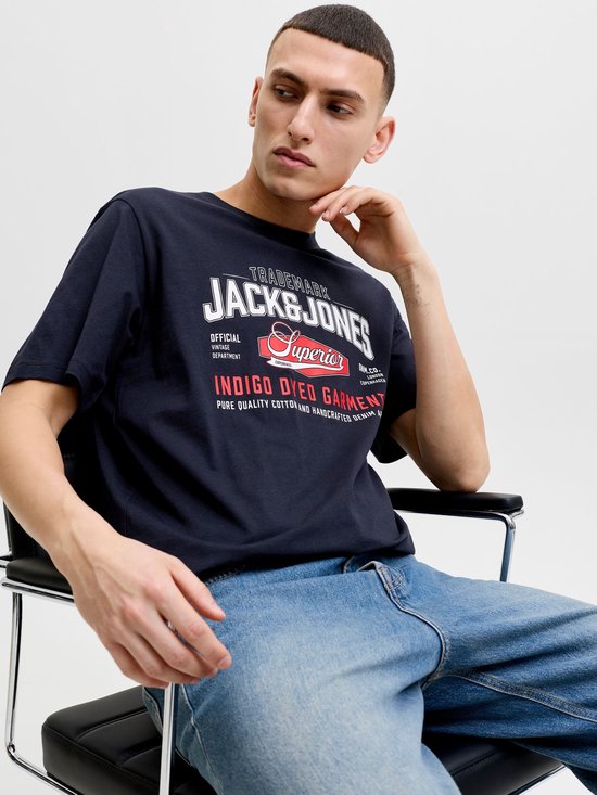 Zittende man in marineblauw T-shirt met 'JACK & JONES' opdruk in wit en rood.