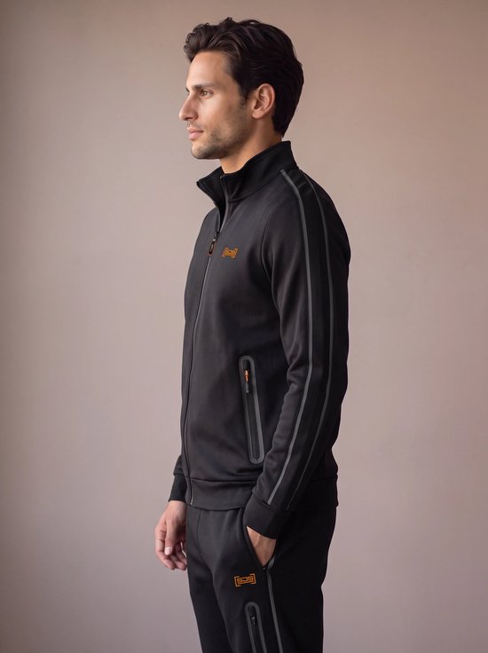 Man in zwart sportvest met grijze accentstrepen en oranje logo op borst en broek.