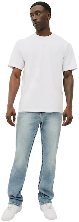 Model draagt een lichtblauwe True Religion Ricky jeans met een wit T-shirt en witte sneakers.