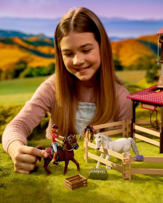 Kind speelt met een bruin speelgoedpaard en een witte pony in een paardenstalset van Schleich.
