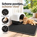 Zwarte kattenbakmat met honingraatstructuur naast een kattenbak met een oranje kat die ernaast ligt.