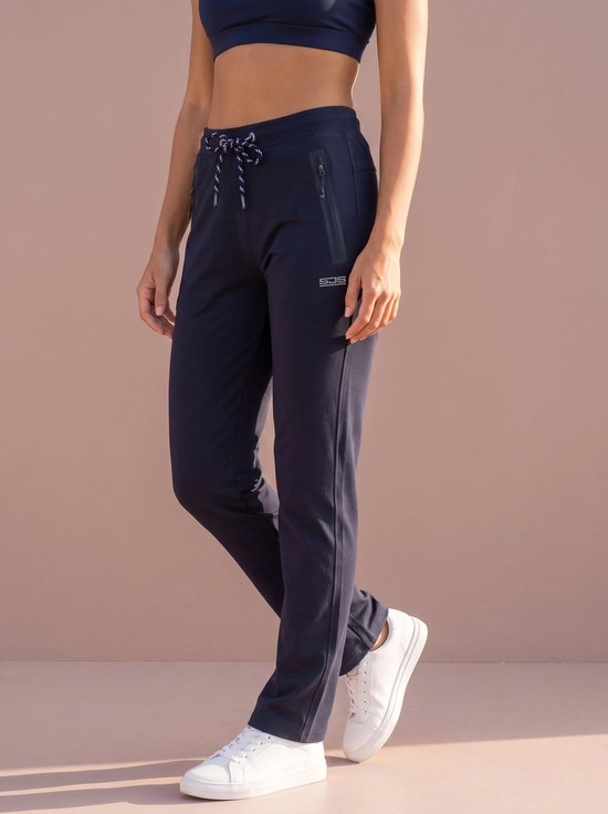 Model draagt marineblauwe Sjeng sportbroek met trekkoord, ritszakken en logo op de heup, gecombineerd met witte sneakers.