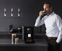Man met lichtblauwe blouse drinkt een espresso naast de zwarte Krups Intuition Preference machine.