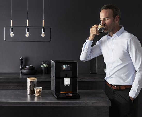 Man met lichtblauwe blouse drinkt een espresso naast de zwarte Krups Intuition Preference machine.