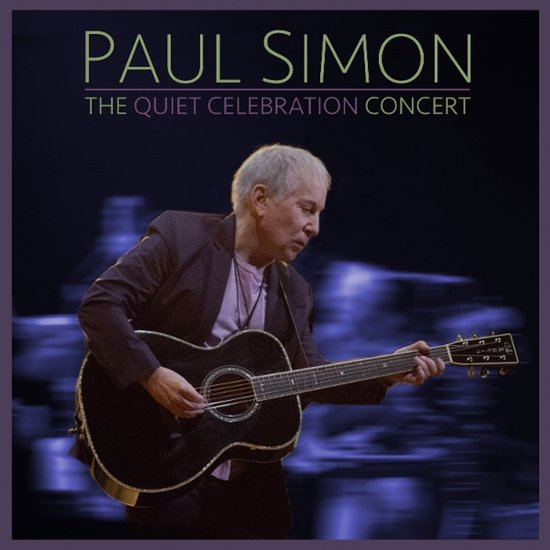Paul Simon speelt akoestische gitaar tijdens "The Quiet Celebration Concert". Hij draagt een donker jasje en een paarse top.