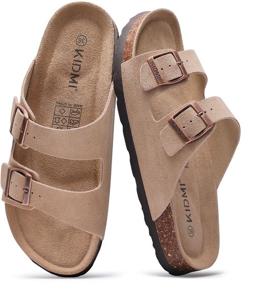 Beige suède slippers met twee bandjes, koperkleurige gespen en bruine kurkzolen.