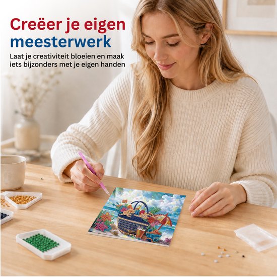 Een vrouw creëert een diamond painting met een mand vol bloemen op een strand, met de steentjes en tool op tafel.
