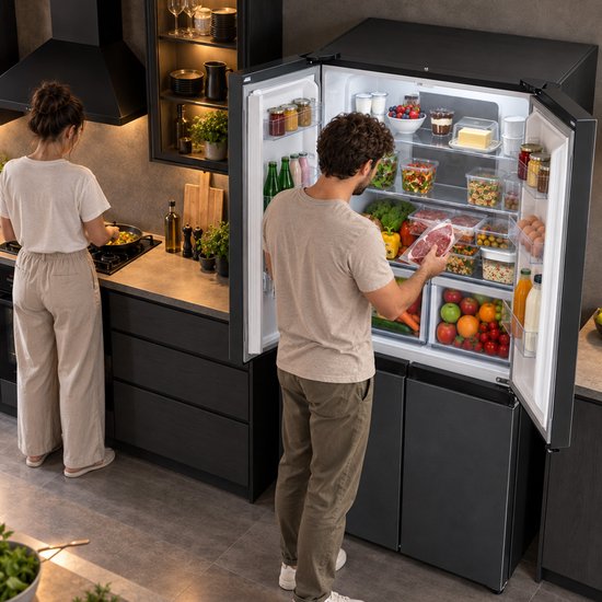 Man pakt een stuk vlees uit een open, donkergrijze Heinner Amerikaanse koelkast in een keuken, terwijl een vrouw kookt.