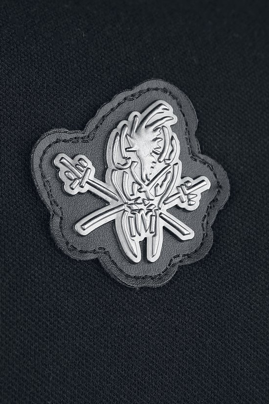 Close-up van een grijze patch op een zwart poloshirt met een gebogen schedel en gekruiste zwaarden.
