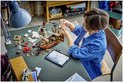 Garçon construisant un navire pirate LEGO avec voiles, canons et figurines sur une table.