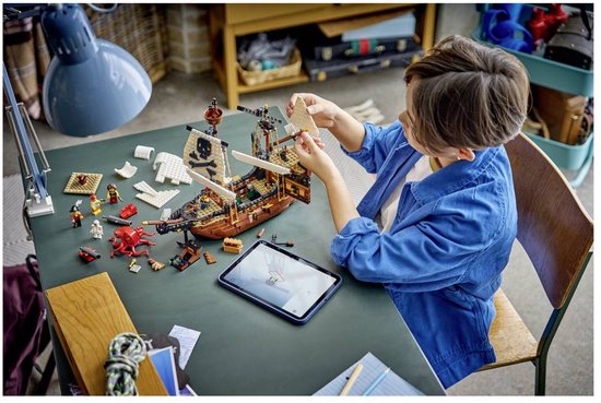 Garçon construisant un navire pirate LEGO avec voiles, canons et figurines sur une table.