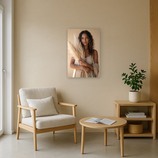 Canvas schilderij van een vrouw met pampasgras, in een neutraal interieur met een fauteuil en ronde tafel.