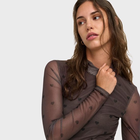 Close-up van model in bruine mesh top met hartjesprint en hoge hals.