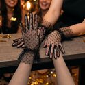 Zwarte tule handschoenen met stippenpatroon en ruches bij de pols, gedragen door een vrouw aan een feesttafel.