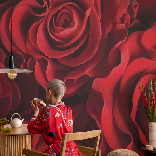 Vrouw in rode kimono met bloemenprint drinkt thee voor een muur met gigantische rode rozen.