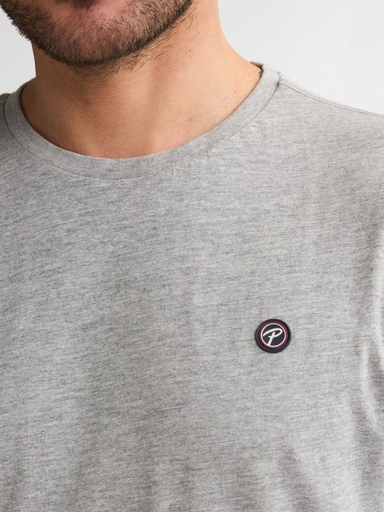 Detailopname van een grijs t-shirt met een ronde hals en een klein, rond logo met de letter P op de borst.