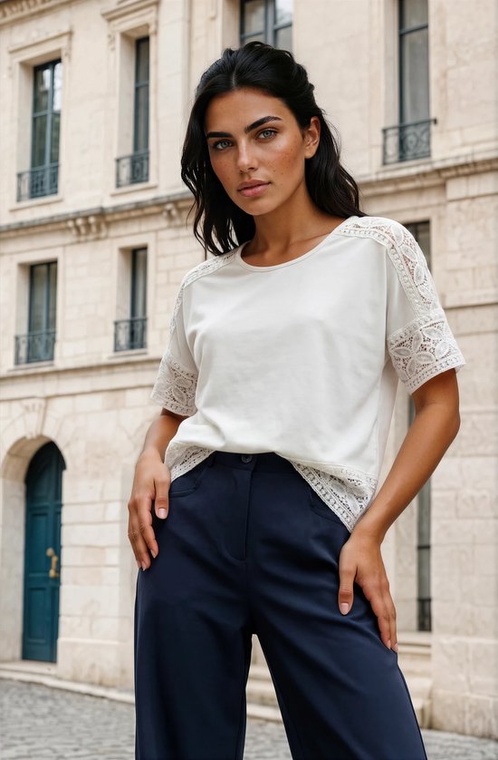 Close-up van model in wit T-shirt met kanten details op de schouders en mouwen, gecombineerd met een donkerblauwe broek.