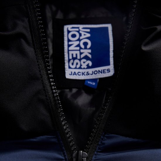 Detail van een blauw-wit 'JACK & JONES' neklabel in een zwarte gewatteerde jas met rits.