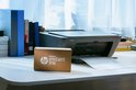 Zwarte HP DeskJet printer op bureau naast een doos met HP Instant Ink-logo.