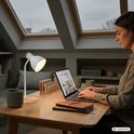 Witte bureaulamp op bureau met persoon die op laptop werkt.